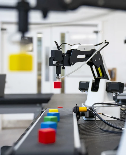 A robotic arm sorting coloured blocks on a conveyor system, demonstrating automation in an advanced engineering lab. A robotic arm sorting coloured blocks on a conveyor system, demonstrating automation in an advanced engineering lab.